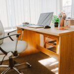 A modern office workspace featuring a wooden desk, chair, laptop, and bright natural light.